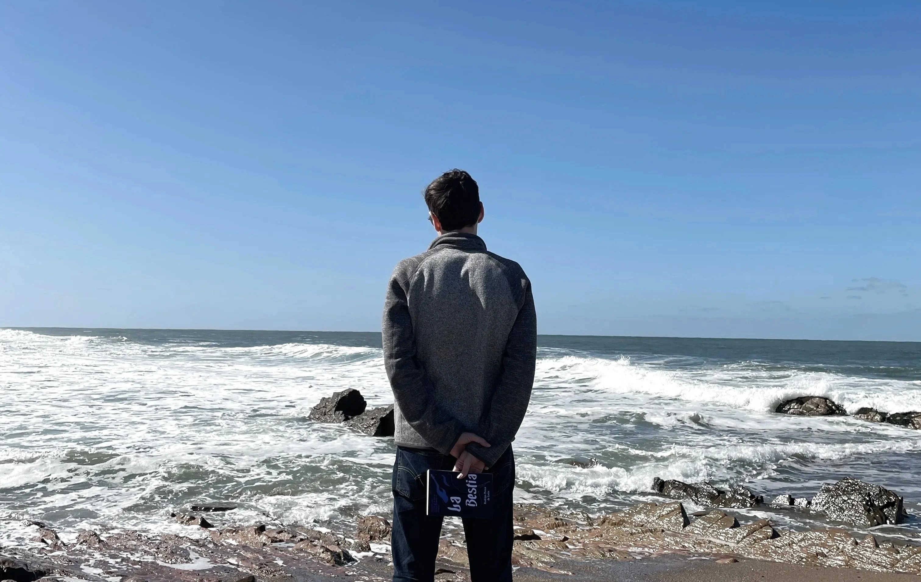 Rodri de espaldas frente al mar, con su libro La Bestia en las manos.